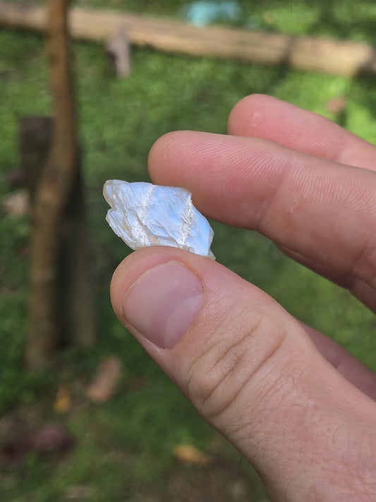 Rough blue moonstone held between two fingers